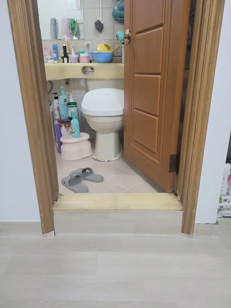 문턱이 낡고 노랗게 변색된 화장실 문 입구 전경
